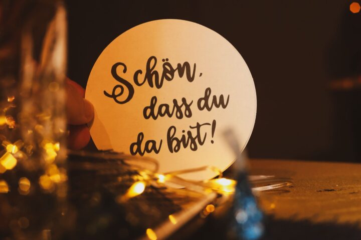 Runder Pappkarton mit der Aufschrift "Schön, dass du da bist!" vor einer festlichen Tischdekoration.