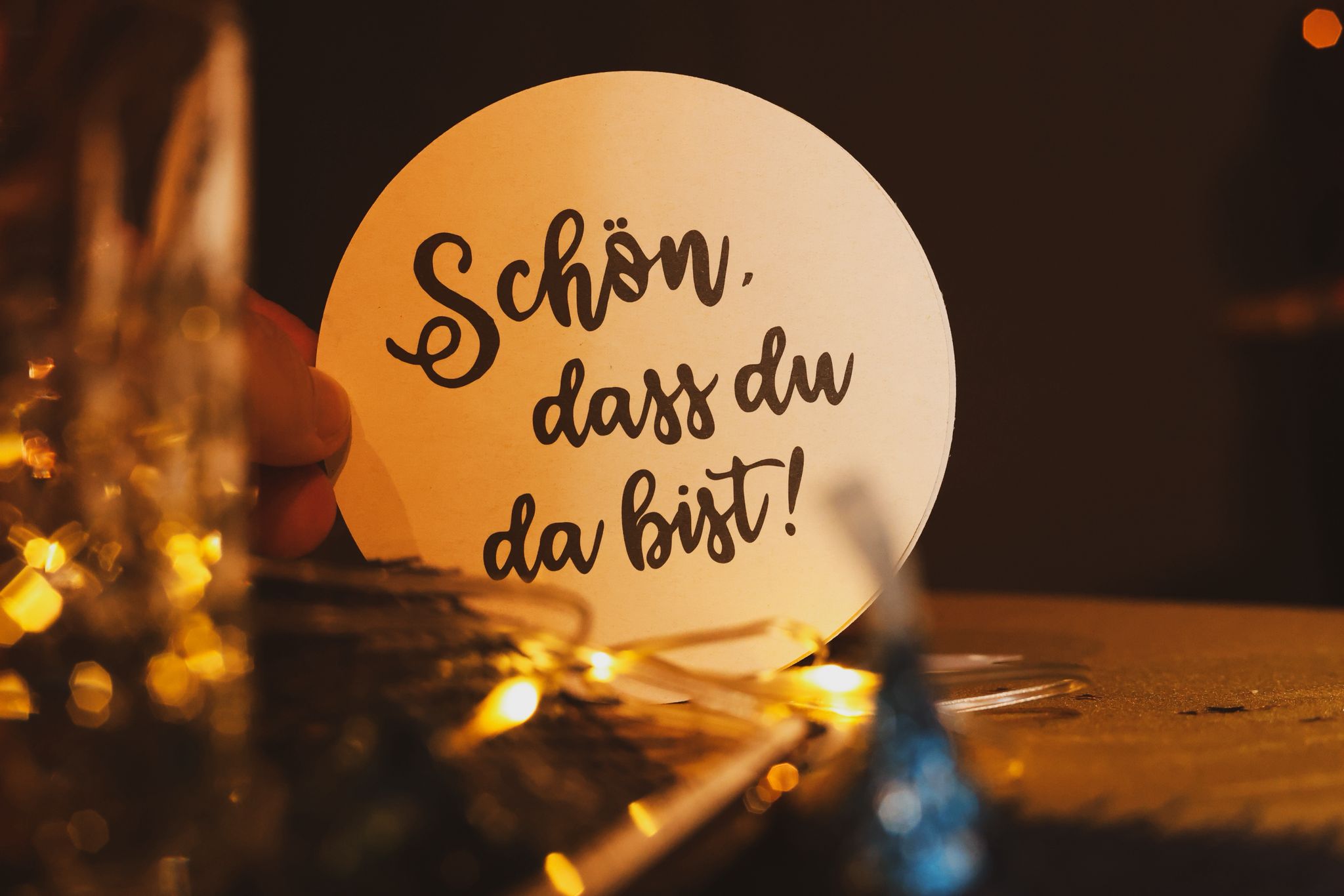 Runder Pappkarton mit der Aufschrift "Schön, dass du da bist!" vor einer festlichen Tischdekoration.