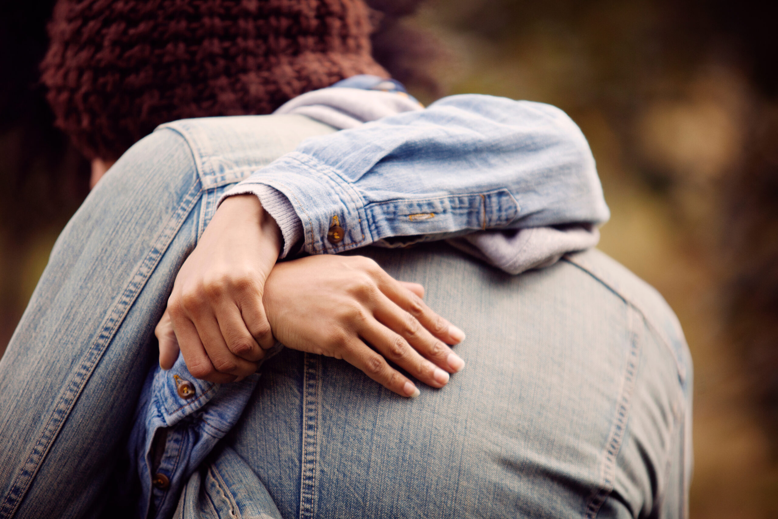 Umarmung zweier Personen in Jeansjacken, eine Hand liegt sanft auf dem Rücken des anderen, vermittelt ein Gefühl von Nähe und Geborgenheit.